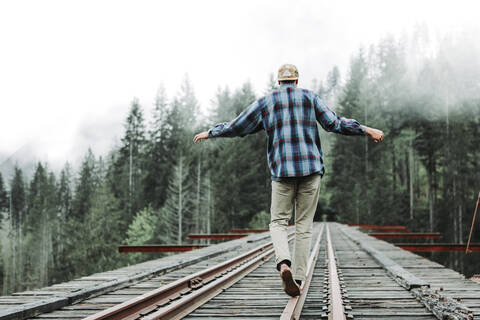 Young man balancing on railroad tracks over bridge in foggy forest stock photo