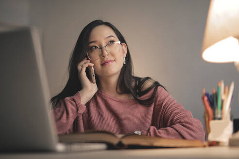 Junge asiatische Frau studiert und telefoniert mit Smartphone von zu Hause aus - CAVF76969