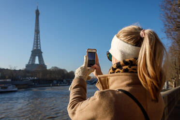 Ein junger Erwachsener macht ein iPhone-Foto vom Eiffelturm in Paris. - CAVF77005