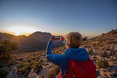 Eine Frau wandert und fotografiert den Berg Puig Campana. - CAVF77020