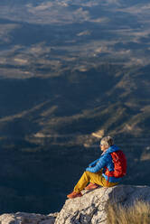 Young woman standing on rocks on top of a mountain looking over. - CAVF77022