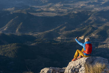 Young woman standing on rocks on top of a mountain making a selfie. - CAVF77025