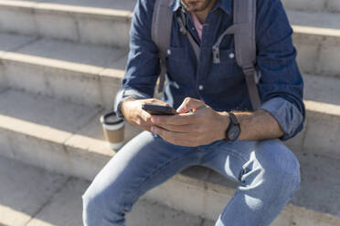 Crop view of man sitting on stairs using smartphone - JPTF00462