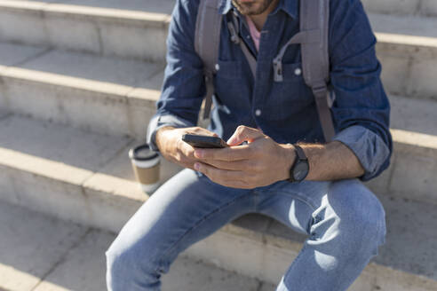 Crop-Ansicht eines Mannes, der auf einer Treppe sitzt und ein Smartphone benutzt - JPTF00462