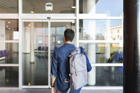 Rückenansicht eines Mannes mit Rucksack vor dem Eingang eines Busbahnhofs - JPTF00468