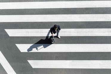 Mann auf dem Zebrastreifen, der seinen Rollkoffer schiebt, Ansicht von oben - JPTF00479