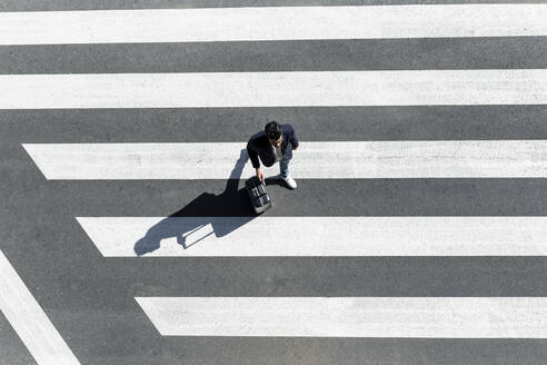 Man on zebra crossing pushing his trolley bag, top view - JPTF00479