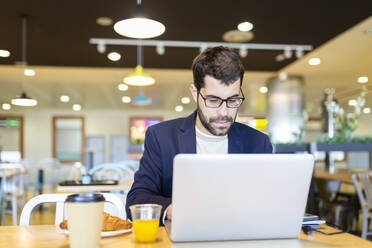 Porträt eines bärtigen Geschäftsmannes, der in einem Café an einem Laptop arbeitet - JPTF00481