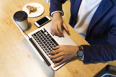 Crop view of businessman working on laptop in a coffee shop - JPTF00485