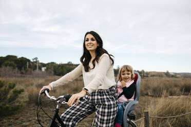 Woman riding bicycle in the countryside with daughter in child's seat - JRFF04128