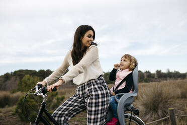 Woman riding bicycle in the countryside with daughter in child's seat - JRFF04129