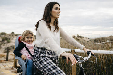 Woman riding bicycle on a boardwalk in the countryside with daughter in child's seat - JRFF04133