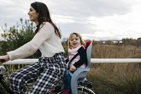 Woman riding bicycle in the countryside with happy daughter in child's seat stock photo