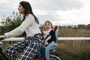Woman riding bicycle in the countryside with happy daughter in child's seat - JRFF04134