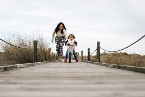 Mutter und Tochter mit Gleichgewichtsfahrrad auf einer Promenade auf dem Lande - JRFF04137