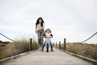 Mutter und Tochter mit Gleichgewichtsfahrrad auf einer Promenade auf dem Lande - JRFF04140