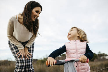 Happy mother looking at daughter with balance bicycle - JRFF04142