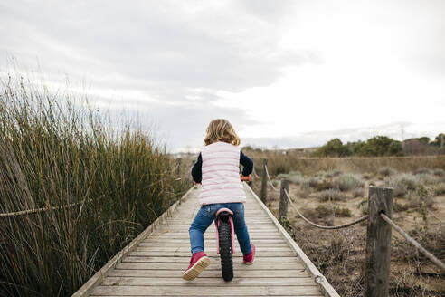 Rückansicht eines kleinen Mädchens mit Gleichgewichtsfahrrad auf einer Promenade auf dem Lande - JRFF04143