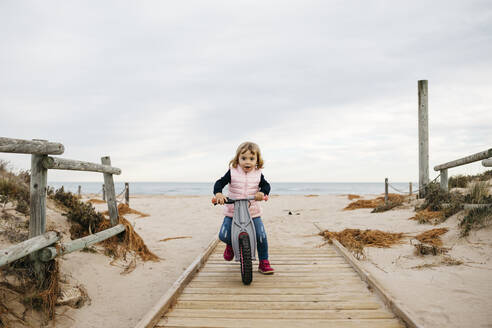 Mädchen im Kleinkindalter mit Gleichgewichtsfahrrad auf einer Strandpromenade in den Dünen - JRFF04148