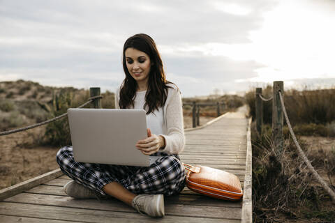Frau sitzt auf einer Promenade auf dem Land und benutzt einen Laptop, lizenzfreies Stockfoto