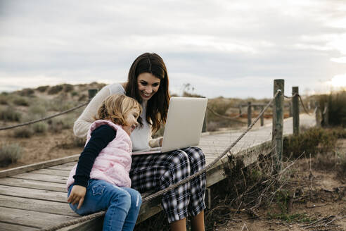 Mutter mit Laptop und Tochter auf einer Strandpromenade auf dem Lande - JRFF04159