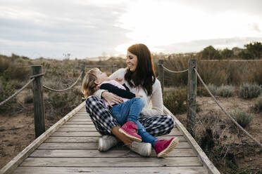 Happy mother and daughter sitting on a boardwalk in the countryside - JRFF04160