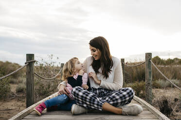 Happy mother and daughter sitting on a boardwalk in the countryside - JRFF04161