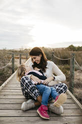 Happy mother and daughter sitting on a boardwalk in the countryside - JRFF04163