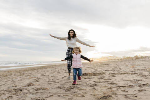 Glückliche Mutter und Tochter spielen bei Sonnenuntergang am Strand, lizenzfreies Stockfoto