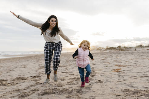 Happy mother and daughter playing on the beach at sunset - JRFF04168