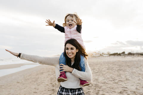 Happy mother carrying daughter on shoulders on the beach at sunset stock photo