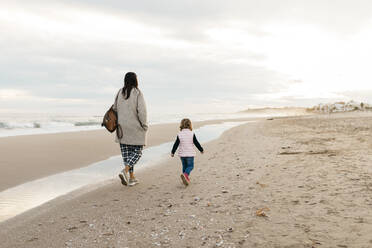 Rückansicht von Mutter und Tochter, die bei Sonnenuntergang am Strand spazieren gehen - JRFF04177