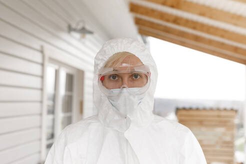 Man in protective clothing, standing in front of house - KMKF01233