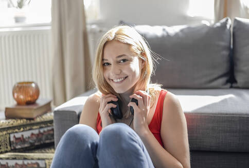 Porträt einer glücklichen jungen Frau, die zu Hause auf dem Boden sitzt und mit Kopfhörern Musik hört - BFRF02201