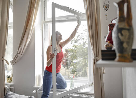 Smiling young woman cleaning window at home - BFRF02202