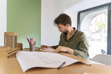 Mann arbeitet an einem architektonischen Modell und einem Plan auf einem Schreibtisch im Büro - AFVF05607