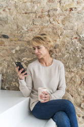 Mature businesswoman having a break sitting on stairs using cell phone - AFVF05644