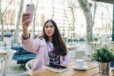 Young woman sitting at outdoor table and taking a selfie - DCRF00112