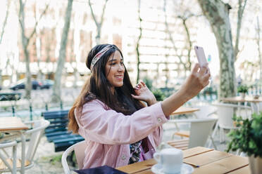 Young woman sitting at outdoor table and taking a selfie - DCRF00113