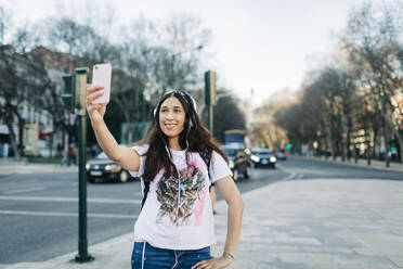 Junge Frau mit Kopfhörern macht ein Selfie mit ihrem Smartphone - DCRF00117