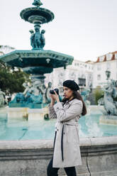 Junge Reisende mit Kamera am Springbrunnen des Rossio-Platzes, Lissabon, Portugal - DCRF00121