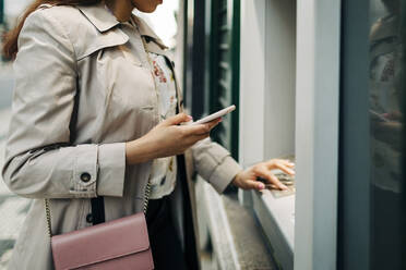 Frau mit Geldautomat und Mobiltelefon - DCRF00123