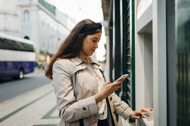 Frau mit Geldautomat und Mobiltelefon - DCRF00124