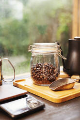 Nahaufnahme von Kaffeekanne, Glasgefäß mit Kaffeebohnen und Metallkaffeeschaufel auf Holzbrett. - MINF14081