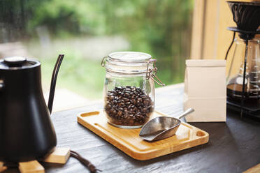Nahaufnahme von Kaffeekanne, Glasgefäß mit Kaffeebohnen und Metallkaffeeschaufel auf Holzbrett. - MINF14082