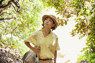 Japanische Frau mit Hut beim Wandern in einem Wald. - MINF14103