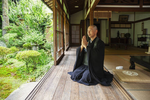 Buddhist priest kneeling in Buddhist temple, praying. - MINF14118