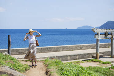 Japanische Frau mit Hut auf einem Weg am Meer. - MINF14129