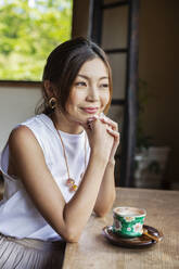 Lächelnde Japanerin, die in einem japanischen Restaurant am Tisch sitzt. - MINF14158