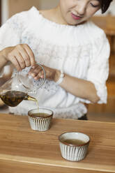 Japanerin sitzt an einem Tisch in einem vegetarischen Café und schenkt Tee ein. - MINF14204